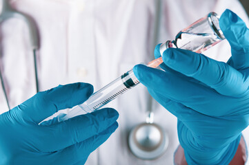 Wall Mural - doctor with stethoscope on the neck and wearing medical glove holding syringe and vial of the vaccine for injection. preventing spread of contagious disease concept. closed up and selective focus