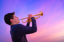 Teen Boy Playing Trumpet Against A Beautiful Sunset Sky