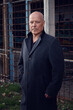 © wernerimages - handsome man in his 50s in black coat standing at an abadnoned buidling