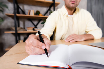 cropped view of freelancer writing in notebook on blurred background