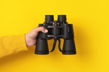 Wall Mural - hand holding binoculars over yellow background