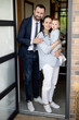 © rh2010 - A portrait of caucasian young family with baby standing in front of their front door house welcoming guest at house. Happy husband and wife with one year old baby boy.