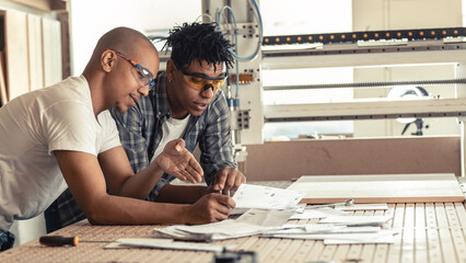 Two black man coworkers, carpenters examining blueprint and checking a list of daily assignment. Preparing for job.	