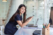 © amnaj - Asian businesswoman sitting in a modern office with a smartphone. Looking at the camera.