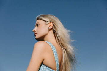 Portrait of a young woman with long blonde hair on blue sky background, outdoors.