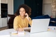 © Face Stock - Cheerful African-American young woman talking on the smartphone, using laptop and taking notes at home, black female freelancer holding phone conversation and making schedule, writes down. Remote work