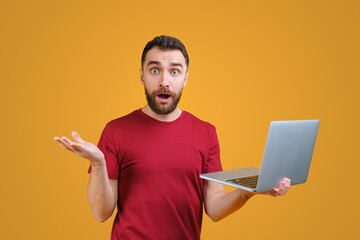 Wall Mural - Young bearded man holding laptop computer in hand and looking directly at the camera with confused face expression