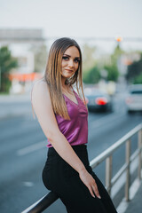 Wall Mural - Vertical shot of a young blonde female model posing on the sidewalk in a pink blouse and black pants