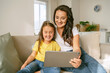 © valeriyakozoriz - Little girl daughter and positive young mother watching funny videos together on digital tablet while relaxing on sofa in living room at home and enjoying family weekend. Kids and modern technologies