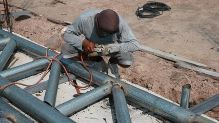 Wall Mural - A welder is sitting on a steel roof frame and is welding steel pipes and wearing masks and leather gloves.