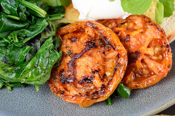 Two slices of grilled tomato on a blue plate with the green spinach to the side