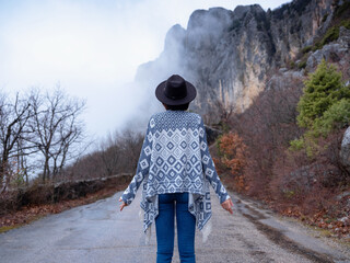 Stylish hipster woman in a hat walking down a mountain road