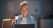 © TommyStockProject - Mature businesswoman working on laptop holding coffee cup at night in office