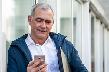 Wall Mural - adult attractive man using mobile phone and holding laptop on the street