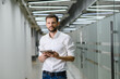 © kalinichenkod - A man in a white shirt holds a tablet and smiles in the office. business man on the background of the office