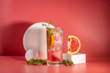 Wall Mural - Highball glass of fresh grapefruit cocktail with ice, rosemary and thyme on pink table surface, art drink concept.