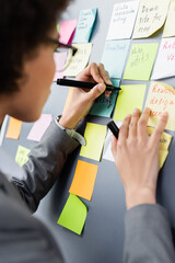 Marker in hand of african american manager near colorful sticky notes on board