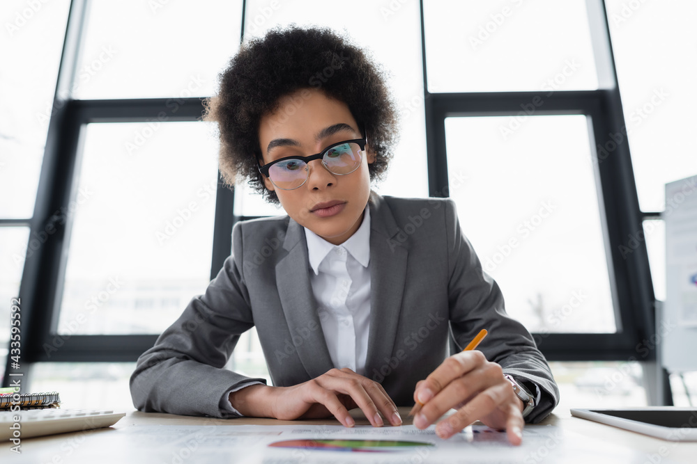 African american businesswoman with pencil working with document on blurred foreground - obrazy, fototapety, plakaty 
