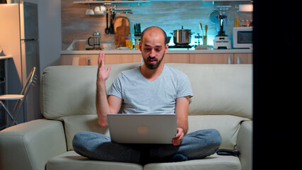 Poster - Focused man talking with business people during online meeting videocall on laptop computer. Caucasian person sitting on sofa late at night using videoconference online web internet communication