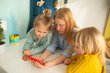 © Ева-Мария Фрей - Children receive education at home in a classroom with a laptop, online courses for kids, three caucasian girls have fun and watch cartoons