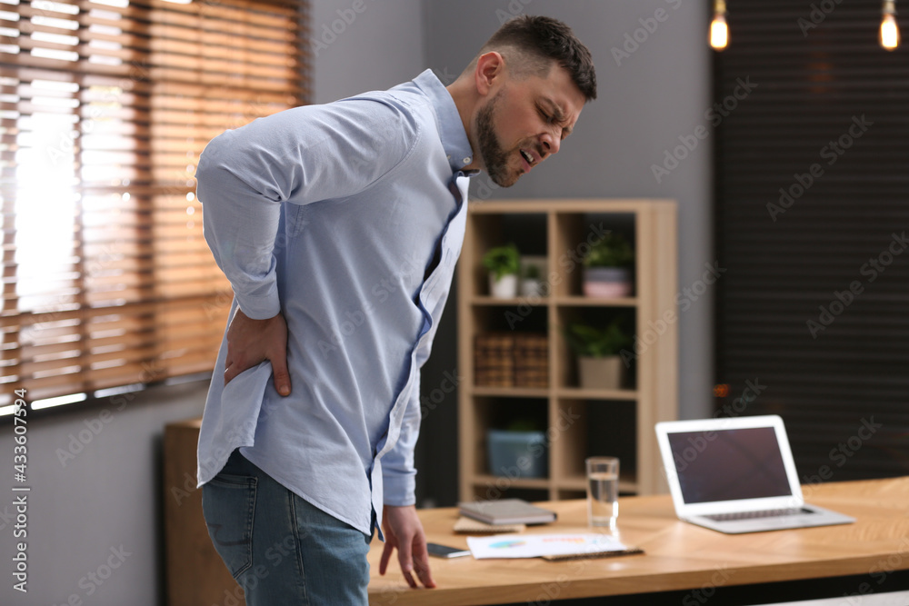 Man suffering from back pain in office. Symptom of poor posture - obrazy, fototapety, plakaty 