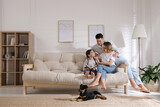 Fototapeta  - Happy family on sofa and puppy in living room