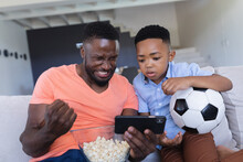 African American Father And Son Sitting On Sofa, Using Samrtphone