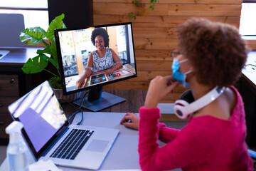 Poster - African american businesswoman wearing face mask sitting at desk using computer having video call