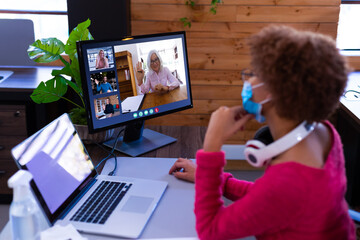 Poster - African american businesswoman wearing face mask sitting at desk using computer having video call