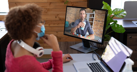 Poster - African american businesswoman wearing face mask sitting at desk using computer having video call