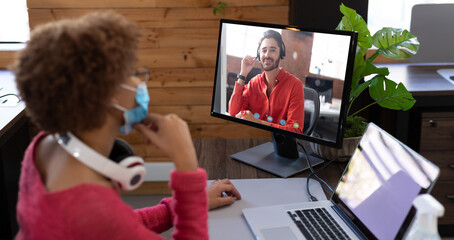 Poster - African american businesswoman wearing face mask sitting at desk using computer having video call