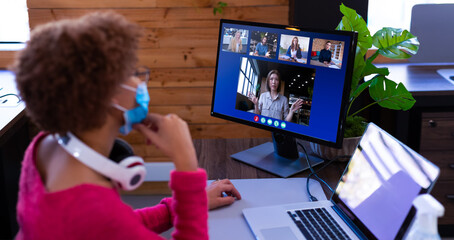 Canvas Print - African american businesswoman wearing face mask sitting at desk using computer having video call