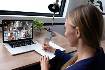 Poster - Caucasian businesswoman sitting at desk using laptop having video call with group of colleagues