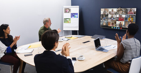 Wall Mural - Diverse group of business colleagues having video call with coworkers on screen in meeting room