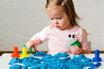 little girl playing with blue kinetic sand. educational games with children for fine motor skills. s
