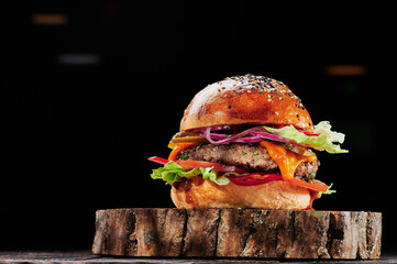 Beef burger with cheese, tomatoes, red onions, cucumber and lettuce on wooden cut on black background. Burger menu. Space for text. Unhealthy food. High quality photo