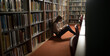 © Wavebreak Media - Caucasian female student with long hair leaning on bookshelf, reading book in library