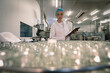 © Wavebreak Media - Caucasian woman wearing lab coat and cap holding clipboard inspecting glassware products in factory