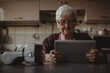 © Wavebreak Media - Portrait of senior woman sitting in kitchen, using tablet