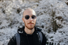 Bearded Male Backpacker Looking At Camera Against Snowy Trees During Journey On Sunny Day