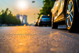 Fototapeta  - Sunset in the city, the empty road with parked cars. Close up view from the level of a parked car wheels