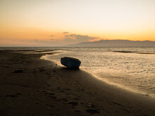 Peaceful Seascape With Old Fishing Boat Moored On Sandy Beach Near Calm Sea At Sunset Time
