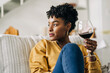 © Jake Jakab/ADDICTIVE STOCK - Content African American female sitting on sofa with glass of red wine and enjoying weekend at home while looking away