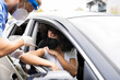 © Jose Carlos Ichiro/ADDICTIVE STOCK - Side view of male doctor in protective uniform, latex gloves and face shield vaccinating African American female patient inside the car on a drive through mobile clinic during coronavirus outbreak