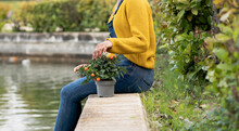 Side View Of Anonymous Black Female Sitting Near Pond In Park With Potted Plant