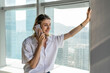 © Luis Gomez/ADDICTIVE STOCK - Young happy businesswoman standing in office with big windows having a phone call on the mobile phone
