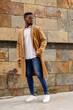 © Sebastian Candiolli/ADDICTIVE STOCK - Full body of African American male wearing trendy coat standing near stone wall of building in city and looking away