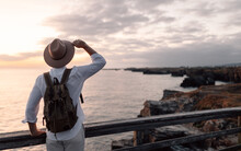 Man With Backpack And Hat Standing On A Walkway Looking At The Sea