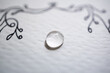 © AnaPliego - Detalle de gota de agua sobre papel con textura blanco y dibujo atrás desenfocado