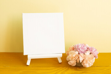 Wall Mural - Blank white canvas with carnation flowers on wooden table. yellow background